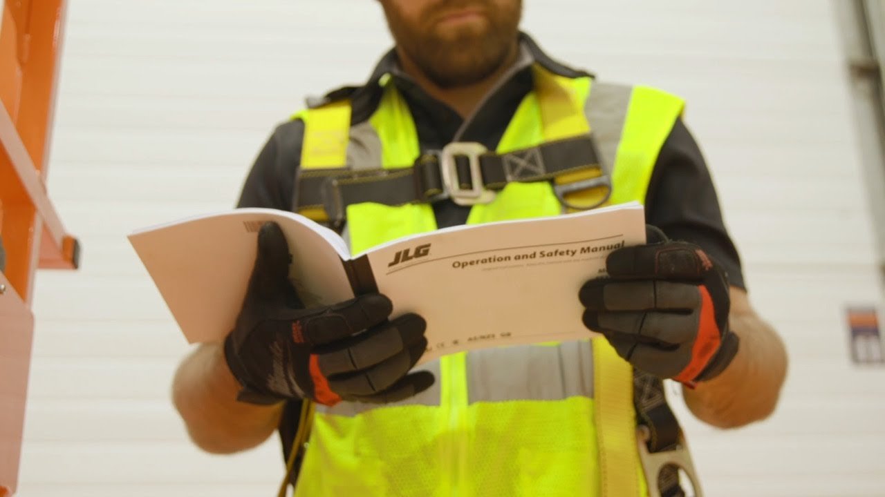 Worker in a hi-vis vest and fall-protection harness reading a safety manual